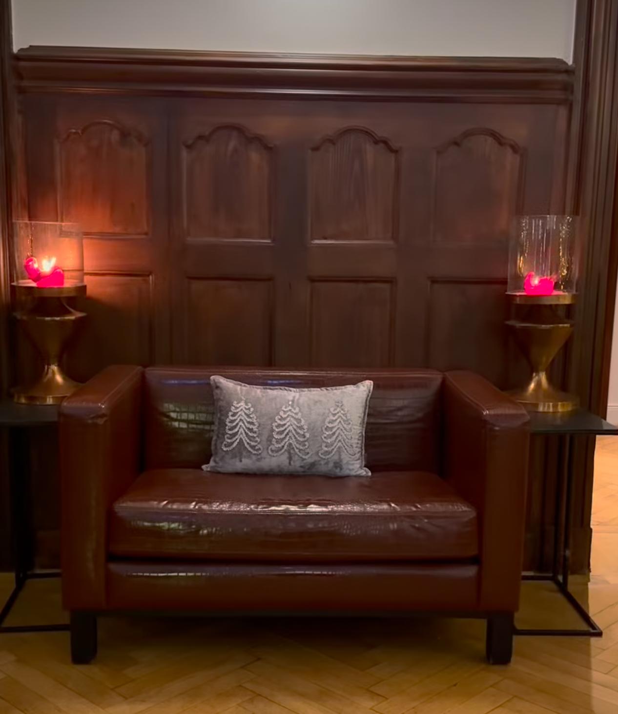 Zweisitzer in cognacfarbenem Leder vor dunkler Holzvertäfelung der Hotellobby.
