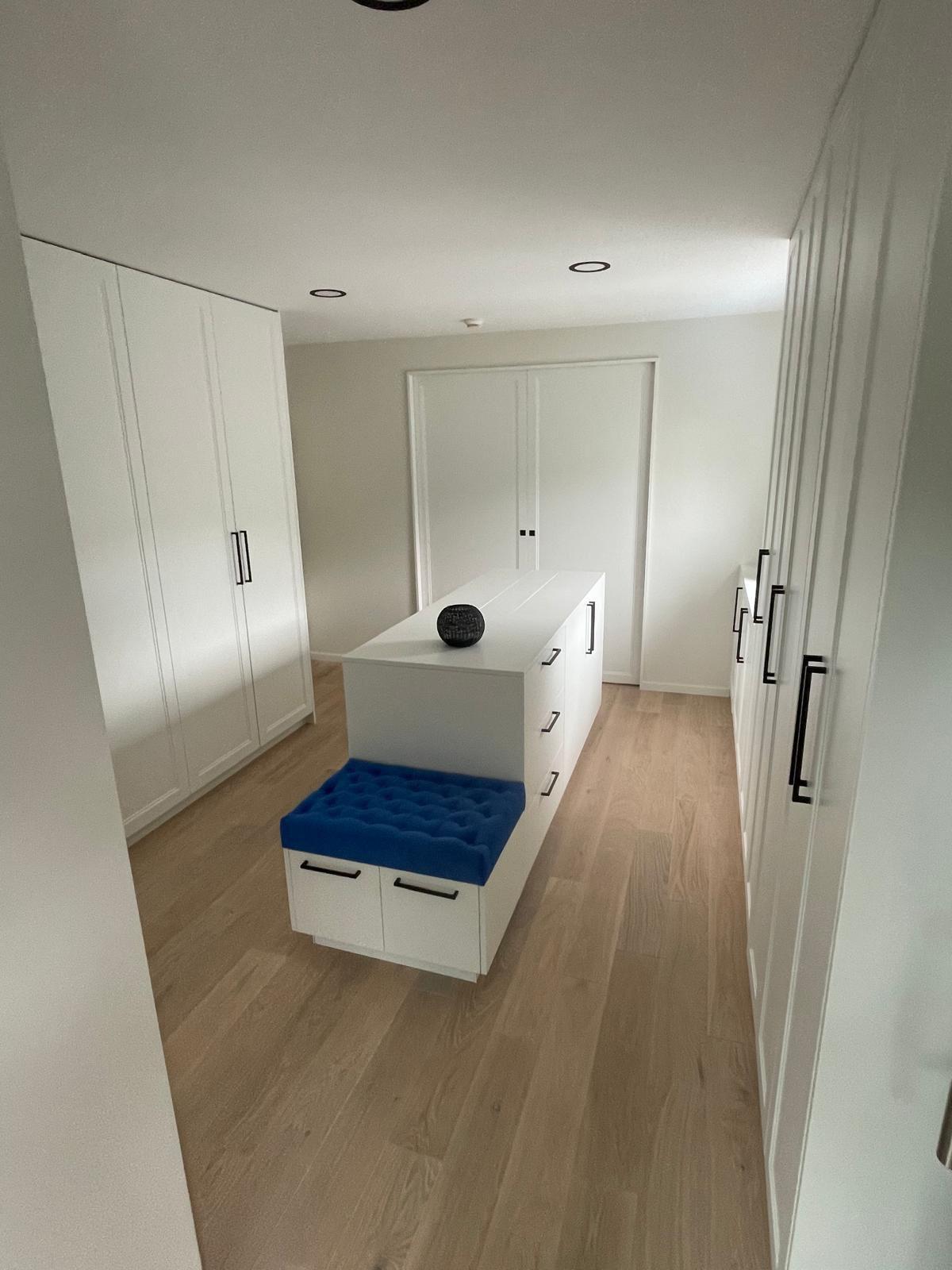 Blau gepolsterter Hocker mit Kapitonage, eingebaut in eine weiße Ankleide.