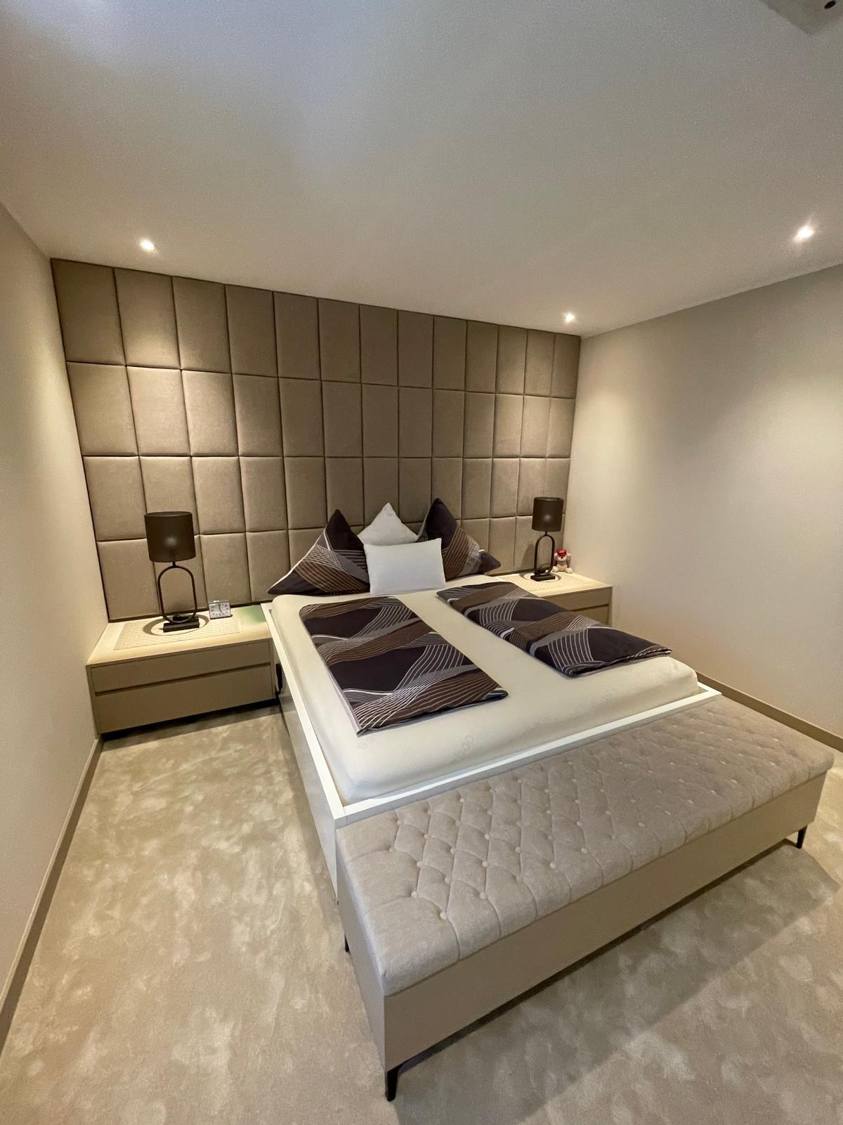 Hotelzimmer mit großflächig gepolsterter Wand hinter dem Bett.