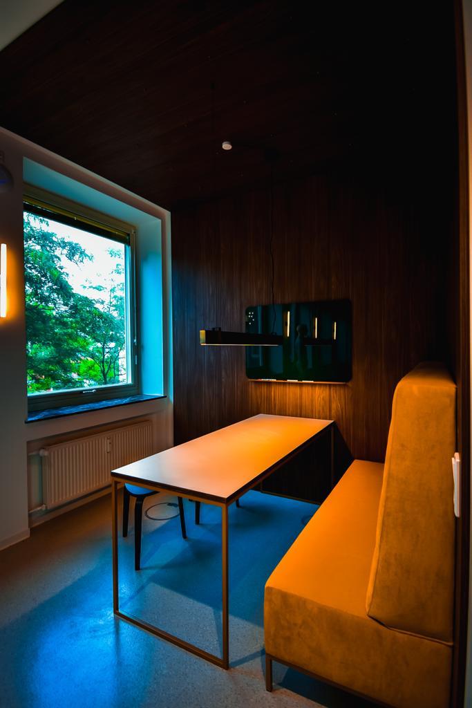 Orangefarbene Hochlehner-Bank neben Fenster und Stehtisch.