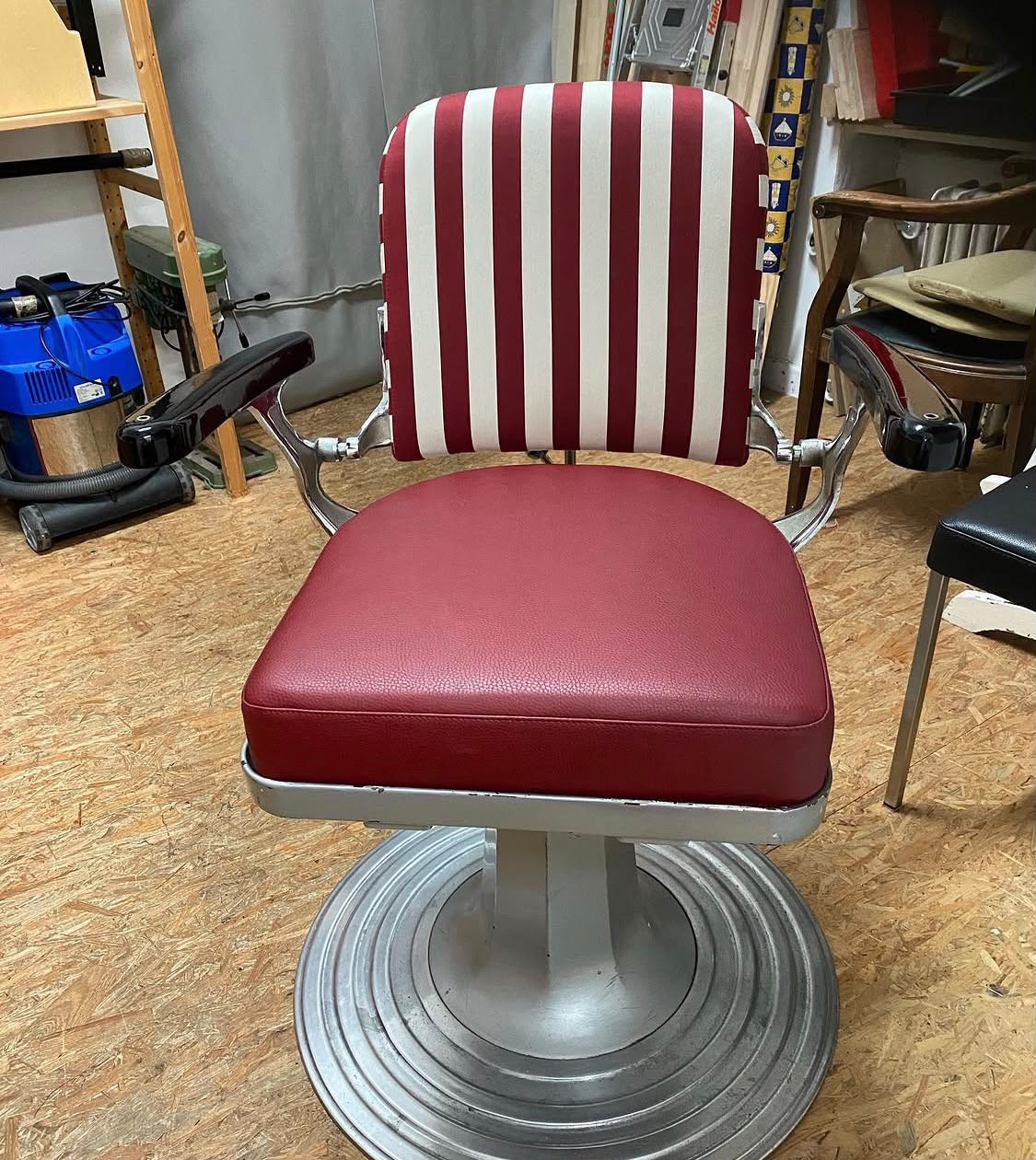 Historischer Friseurstuhl mit rot-weiß gestreifter Lehne und dunkelrotem Ledersitz, fertig in der Werkstatt.