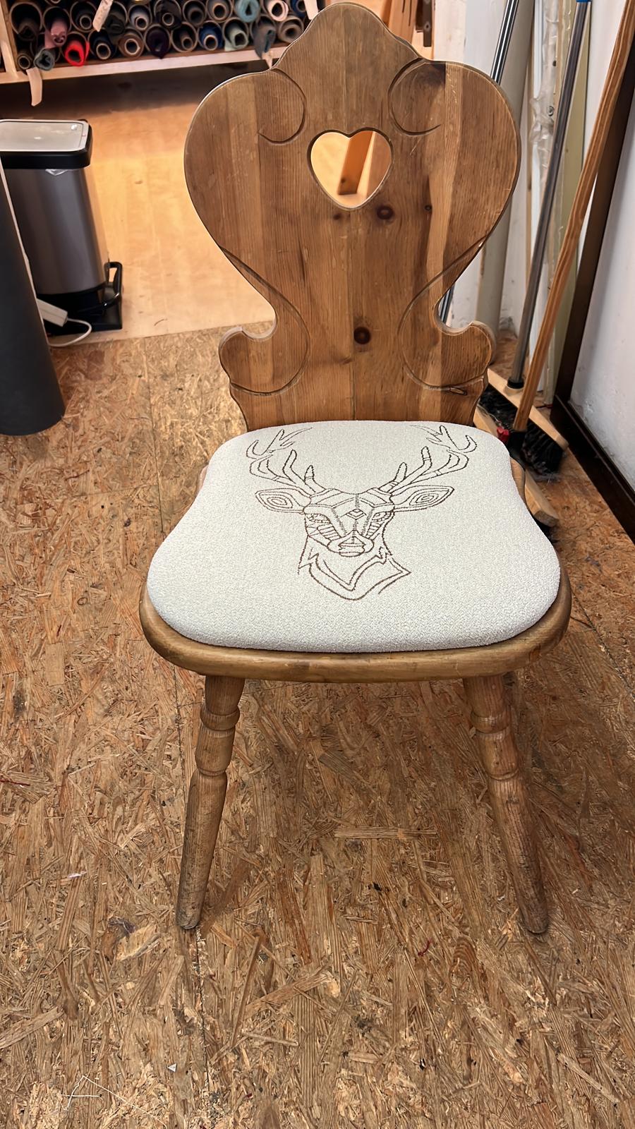 Gepolstertes Sitzkissen aus hellem Bouclé mit Hirschmotiv auf einem Brettstuhl.