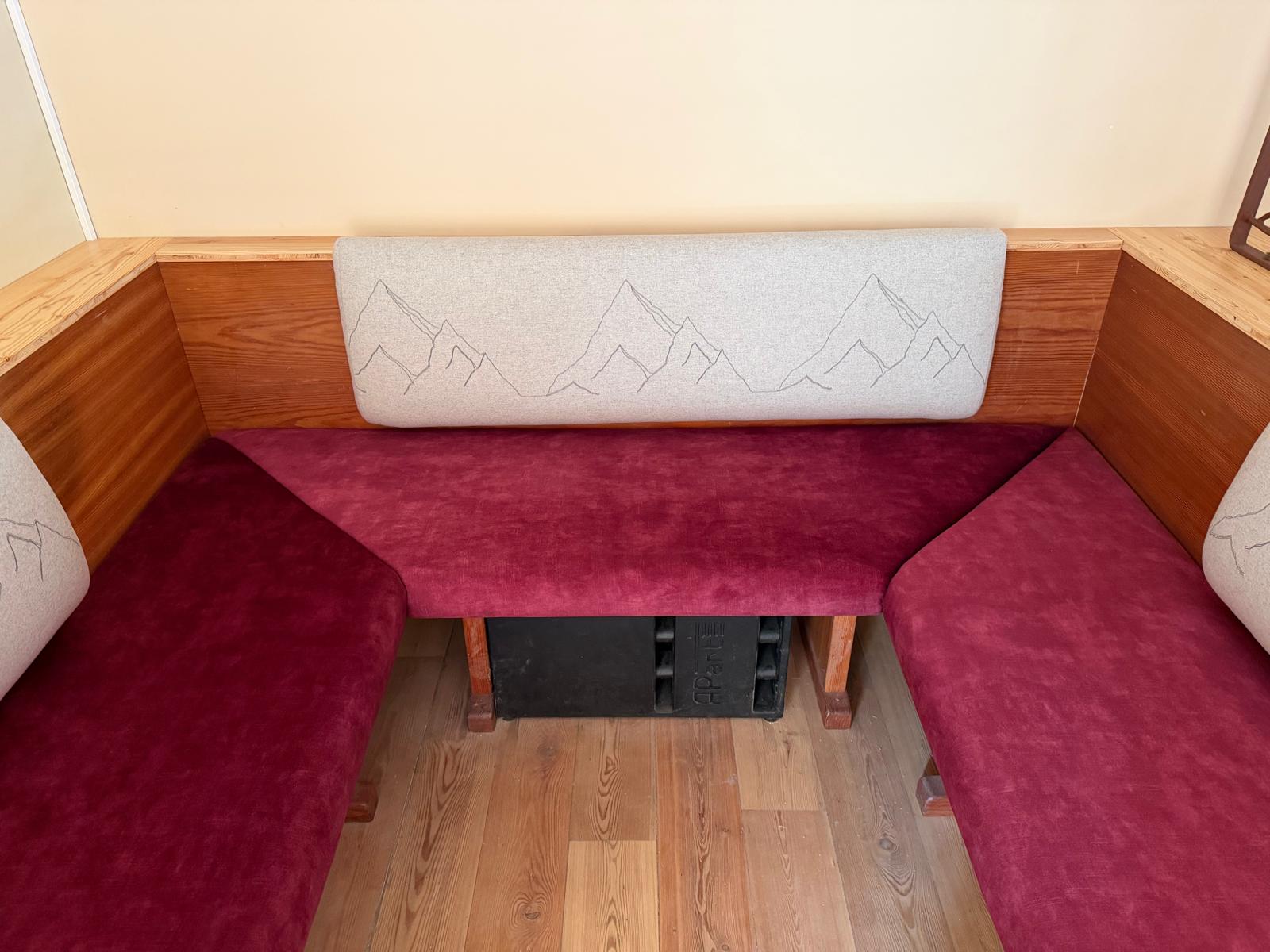 Sitzbank in Beere mit cremefarbenem Rückenpolster und eingearbeitetem Bergmotiv.